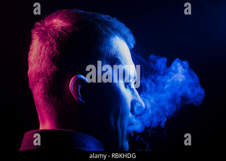 Eine Ansicht von der Rückseite eines jungen Kopf um in einem T-Shirt eine Zigarette und Ausatmen mehrfarbige Rauch von Blau auf der rechten Seite von sich selbst auf Stockfoto