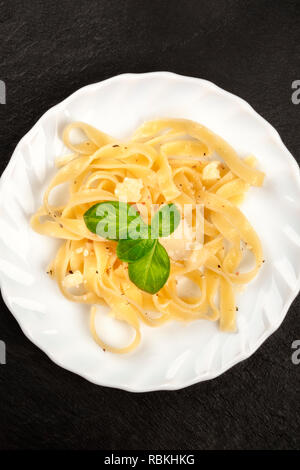 Eine Nahaufnahme von einem Teller Pasta mit geriebenem Parmesan und frischem Basilikum Blätter, geschossen von oben auf einem schwarzen Hintergrund mit Kopie Raum Stockfoto