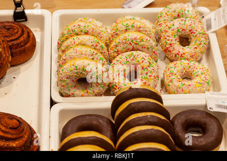 Сlose der frisch gebackenen Krapfen mit Schokoladenglasur und Konfetti auf ein Schaufenster in die Backwaren Abschnitt von einem Einkaufszentrum entfernt. Kein hea Stockfoto