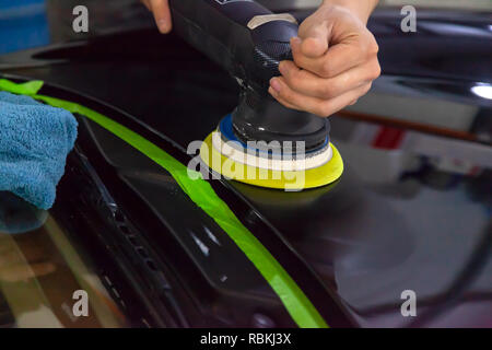 Nahaufnahme auf die Hände eines Mannes, der Arbeiter, der hält ein Werkzeug zum Polieren die Motorhaube eines Autos während der Arbeit in einem Fahrzeug mit Werkstatt. Stockfoto