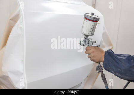 Ein Auto Handwerker bei der Arbeit zur Festsetzung in einer Box hält in seiner Hand ein Werkzeug spritzen mit der Technologie weiter Transport Farbe auf den vorbereiteten weiße Tür Stockfoto