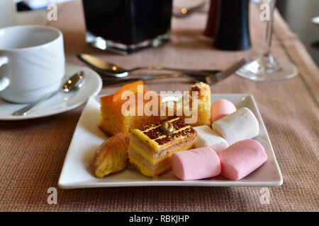 Satz von Süßigkeiten auf weißen Teller am Tisch im Cafe Stockfoto