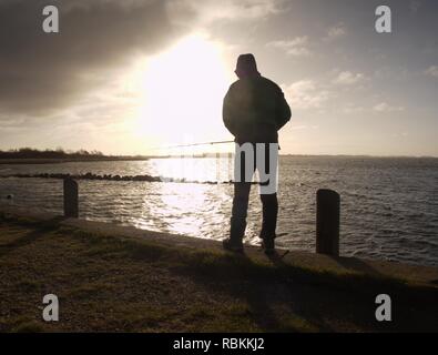 Angler Angeln am Meer Pier, Ansicht schließen. Herbst Marine in der Morgendämmerung. Silhouette der Mann mit Angel in der Hintergrundbeleuchtung Stockfoto