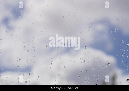 Regentropfen auf dem Fenster; verschwommen weiße Wolken im Hintergrund; geringe Tiefenschärfe Stockfoto