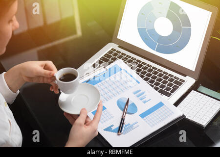 Geschäftsfrau holding Becher Kaffee und mit Diagrammen vertraut Stockfoto