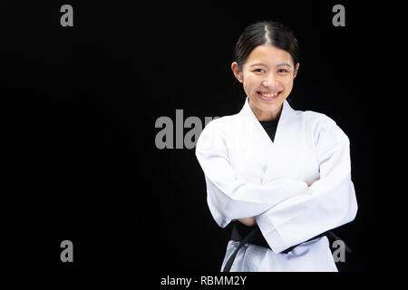 Junge Frau in Karate Anzug Kreuzung Arme mit Happy Face auf schwarzem Hintergrund Stockfoto