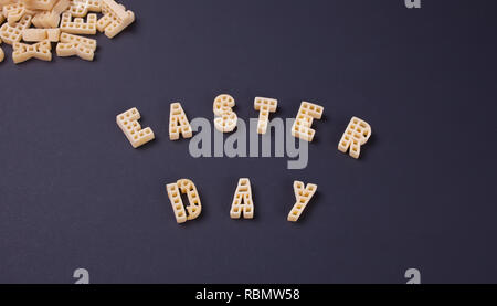 Text Ostern Tag mit Makkaroni in Form von Buchstaben auf schwarzem Holz- Tabelle geschrieben. Ansicht von oben. Stockfoto