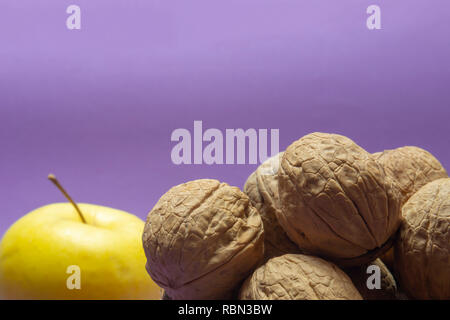 Gesamten gemeinsamen Walnüsse mit Schale in natürlichen Coconut shell Cup und gelber Apfel auf lila Hintergrund Stockfoto