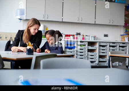 Junge weibliche Grundschullehrerin arbeitet auf einer mit einer Schülerin an Tisch in einem Klassenzimmer sitzen, selektiven Fokus Stockfoto