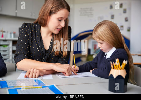 Weibliche Lehrer an einem Tisch sitzen in einem Klassenzimmer mit einem Schulmädchen, ihr zu helfen mit ihrer Arbeit, selektiver Fokus Stockfoto