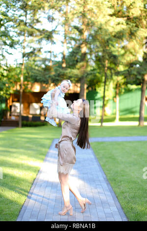 Junge hübsche Frau tragen Kleid Holding Baby im Garten. Stockfoto