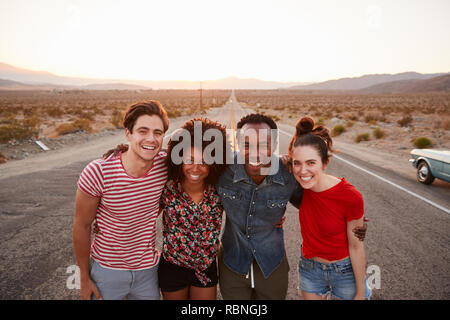 Vier Freunde auf einer einsamen Landstraße lächelnd in die Kamera, in der Nähe Stockfoto