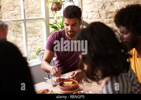 Junge gemischte Rasse Mensch essen mit Freunden an einem Esstisch Stockfoto