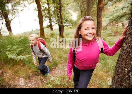 Vor - jugendlich Mädchen eine Pause lehnte sich an einem Baum in einem Wald, ihr Bruder im Hintergrund