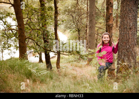 Vor - jugendlich Mädchen steht lehnte sich an einem Baum in einem Wald, durch hohes Gras gesehen Stockfoto