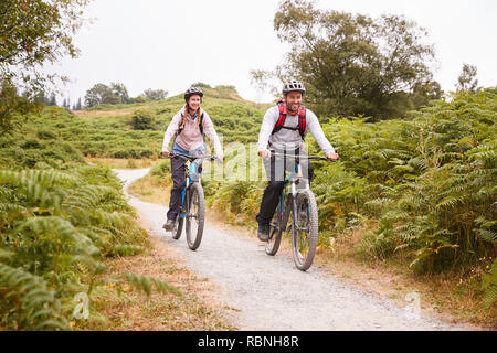 Junge Erwachsene paar Riding Mountain bikes in der Landschaft, volle Länge Stockfoto