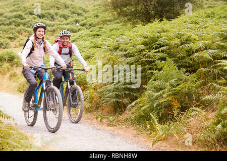 Junge Erwachsene paar Riding Mountain bikes in der Landschaft, volle Länge