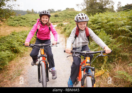 Zwei Kinder reiten Mountain Bikes auf einem Feldweg, Lachen, Vorderansicht Stockfoto