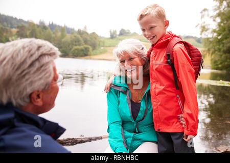 Pre-teen Boy stand neben seinem Großeltern, sitzen am Ufer eines Sees, Lake District, Großbritannien Stockfoto