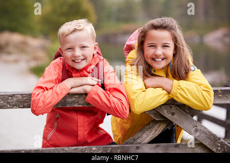 Zwei Kinder lehnte sich auf einem hölzernen Zaun in der Landschaft lächelnd in die Kamera, in der Nähe Stockfoto