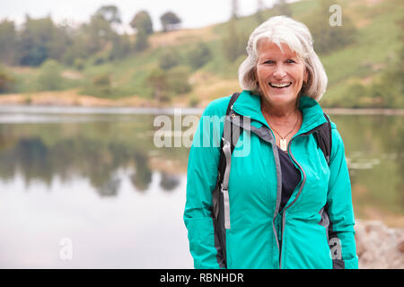 Senior kaukasische Frau, die an einem Ufer eines Sees lächelnd in die Kamera, Porträt Stockfoto