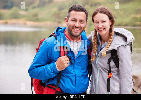 Junge erwachsene Paare auf einer kampierenden Reise in der Nähe von einem See zu Kamera suchen, Nahaufnahme, Lake District, Großbritannien Stockfoto