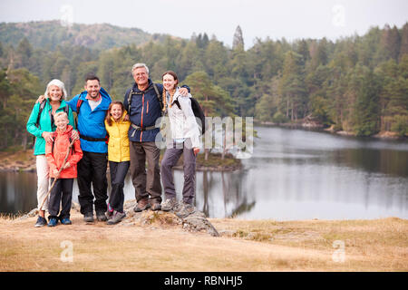 Multi-generation Familie stehen, an einem See, ein Lächeln für die Kamera, Vorderansicht, Lake District, Großbritannien Stockfoto