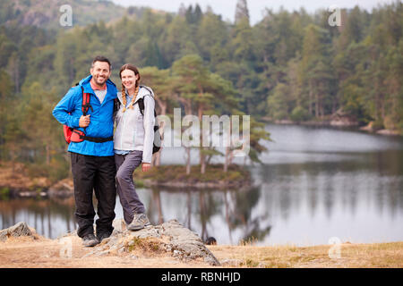 Junge Erwachsene Paar steht auf einem Felsen an einem See im Hinterland, Lächeln für die Kamera, volle Länge Stockfoto