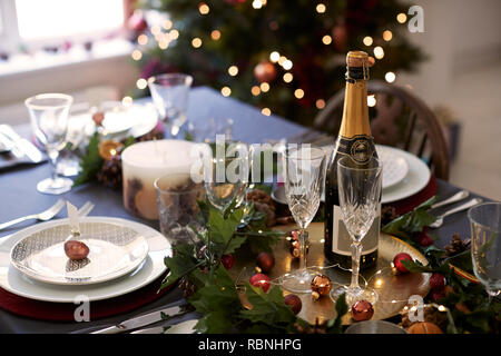 Weihnachten Tisch mit Gläsern und einer Flasche Champagner, christbaumkugel Name Kartenhalter auf einer Platte und Grün und Rot Tischdekoration angeordnet Stockfoto