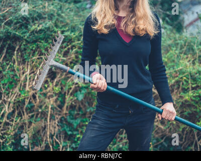 Eine junge Frau steht in einem Garten mit einem Rechen Stockfoto