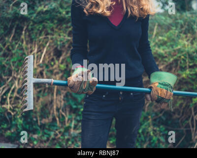 Eine junge Frau steht in einem Garten mit einem Rechen Stockfoto