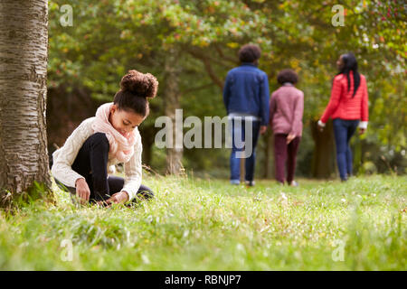 Gemischte Rasse Mädchen im Park kniend ihr Schuh zu binden, ihre Familie wandern in den Hintergrund, die niedrigen Winkel Stockfoto