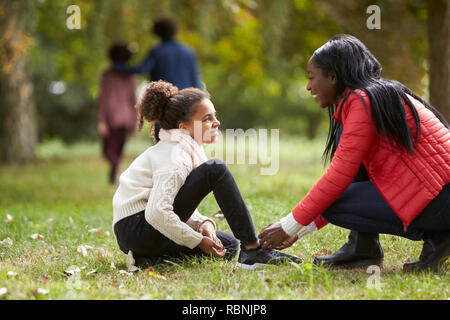 Junge schwarze Frau, die ihre Tochter zu helfen, ihre Schuhe während einer Familie Spaziergang im Park, niedrigen Winkel zu binden Stockfoto