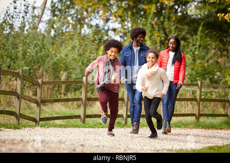 Gemischten rennen Kinder vor ihren Eltern auf einem Pfad während Familie Spaziergang auf dem Land, in der niedrigen Winkel Stockfoto