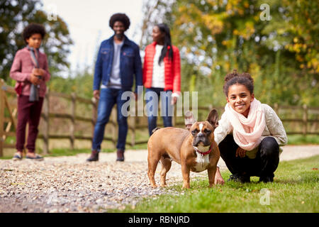 Mischlinge Kauerndes Mädchen zu streicheln, ihr Hund während einer Familie zu Fuß in die Landschaft zu Kamera suchen, niedrigen Winkel Stockfoto