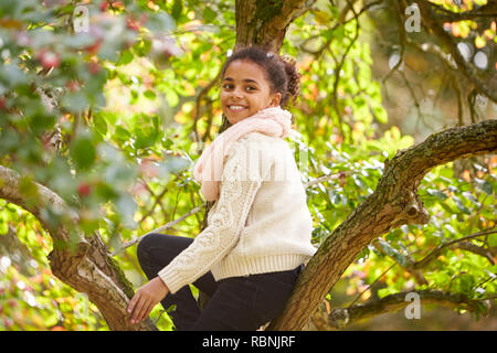 Junges Mädchen sitzt in einem Herbst Baum, drehen und lächelnd in die Kamera, Seitenansicht Stockfoto