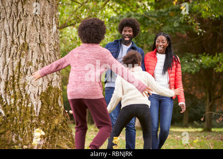 Zwei Kinder springen von hinter einem Baum ihre Eltern bei einem Spaziergang im Park, Ansicht von hinten zu überraschen Stockfoto