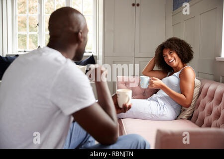 Junge Erwachsene schwarze Frau sitzt auf einer Couch trinken Kaffee an ihrem Partner lächelnd, selektiven Fokus Stockfoto