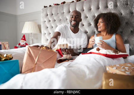 Glückliche junge schwarz Paar im Bett sitzen, die Geschenke auf Weihnachten Morgen, niedrigen Winkel Stockfoto