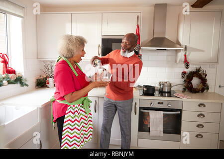 Älteren schwarzen Mann gießen Champagner für seine Partner in der Küche bei der Vorbereitung Abendessen am Weihnachtstag, Seitenansicht Stockfoto