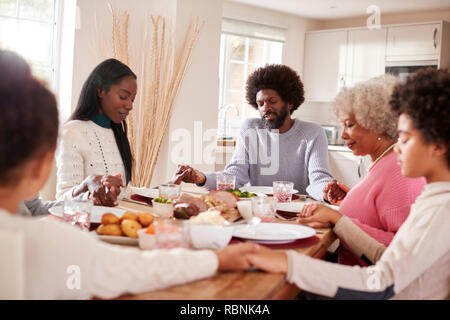 Multi-Generation gemischten Rennen Familie halten sich an den Händen und sagen Gnade vor dem Essen ihren Sonntag Abendessen Stockfoto