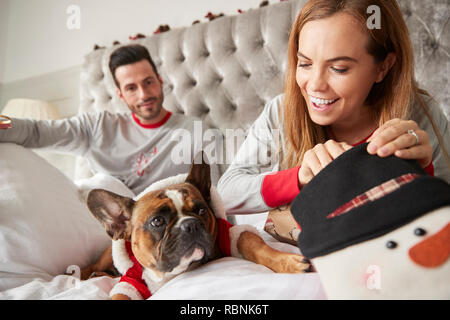 Paar im Bett zu Hause mit Hund gekleidet in Santa Kostüm öffnen Geschenke an Weihnachten Stockfoto