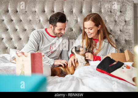 Paar im Bett zu Hause mit Hund Kostüm öffnen Geschenke an Weihnachten Stockfoto