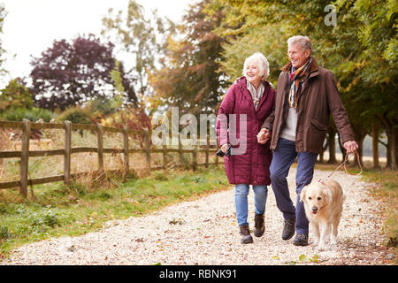 Active Senior Paar auf Herbst Spaziergang mit Hund auf dem Weg durch die Landschaft Stockfoto