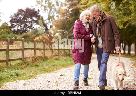 Active Senior Paar auf Herbst Spaziergang mit Hund auf dem Weg durch die Landschaft Stockfoto