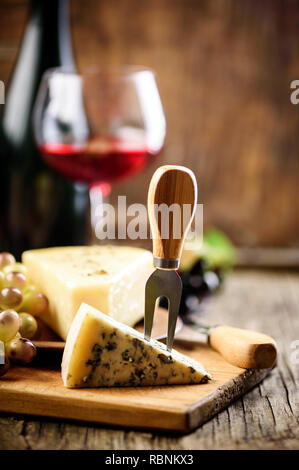 Wein und Speisen im Restaurant. Glas Rotwein und blauen Käse mit Trauben auf rustikalen Holztisch. Stockfoto