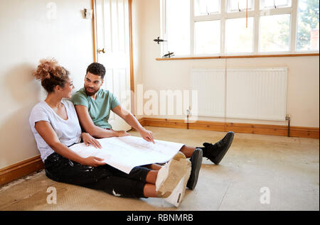 Paar sitzen auf dem Boden an Pläne im leeren Raum der neuen Home Suchen Stockfoto