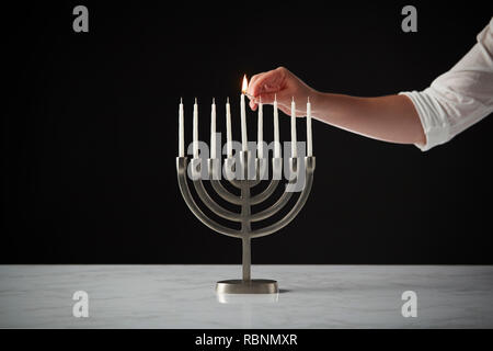 Beleuchtung Kerze auf Metall Hanukkah Menorah auf Marmor Oberfläche gegen Schwarz Studio Hintergrund Stockfoto