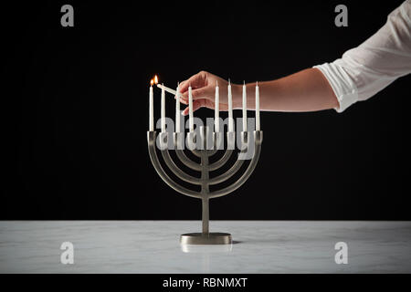 Beleuchtung Kerze auf Metall Hanukkah Menorah auf Marmor Oberfläche gegen Schwarz Studio Hintergrund Stockfoto