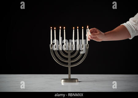 Beleuchtung Kerze auf Metall Hanukkah Menorah auf Marmor Oberfläche gegen Schwarz Studio Hintergrund Stockfoto